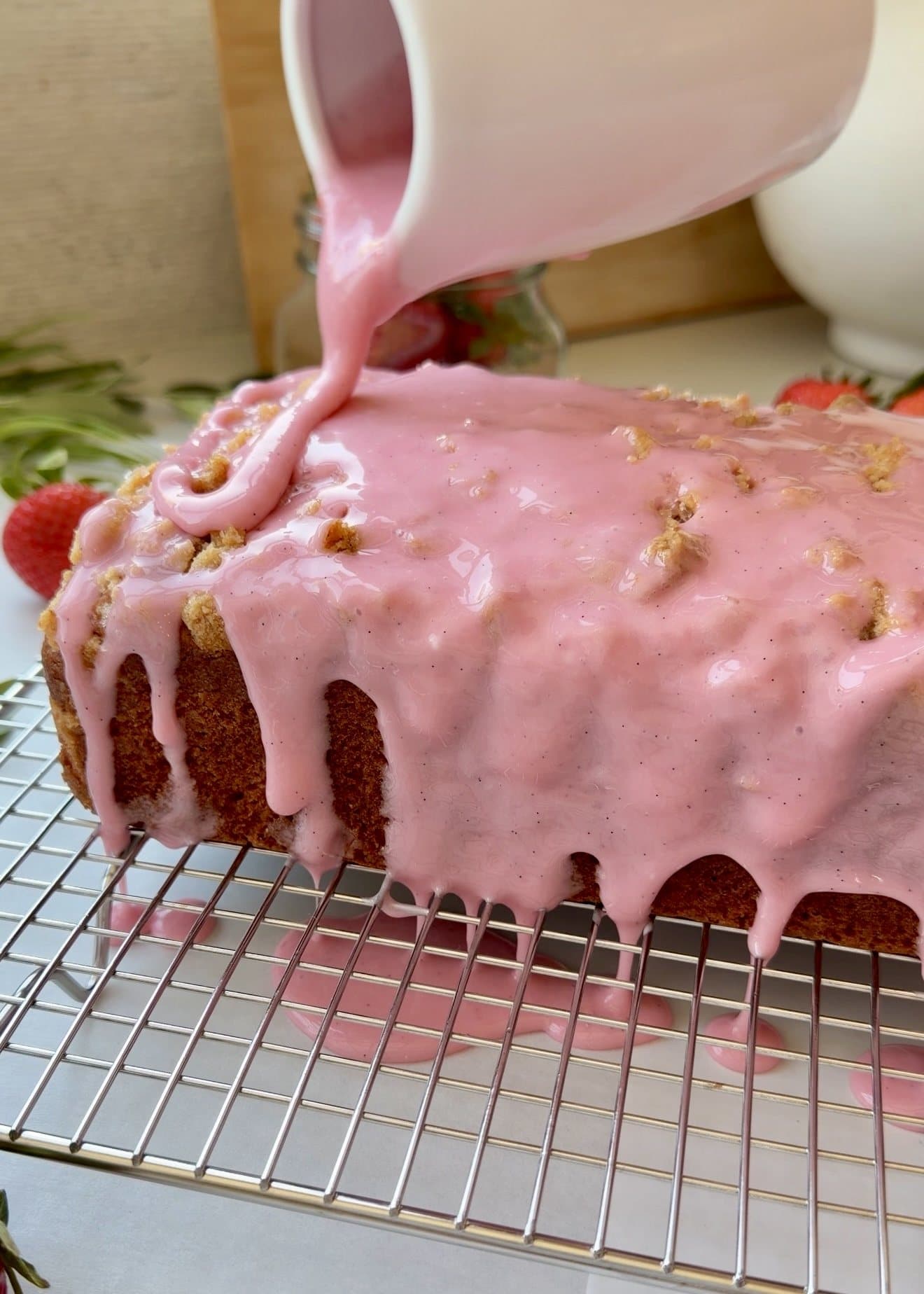 Pink vanilla glaze being poured over a strawberry old-fashioned donut loaf