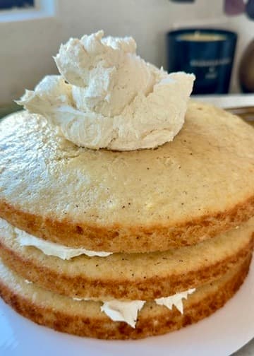 A dollop of buttercream on top of three stacked vanilla cake layers