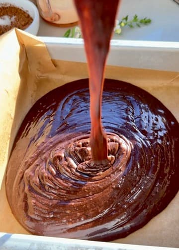 Chocolate cake batter pouring into a parchment-lined pan