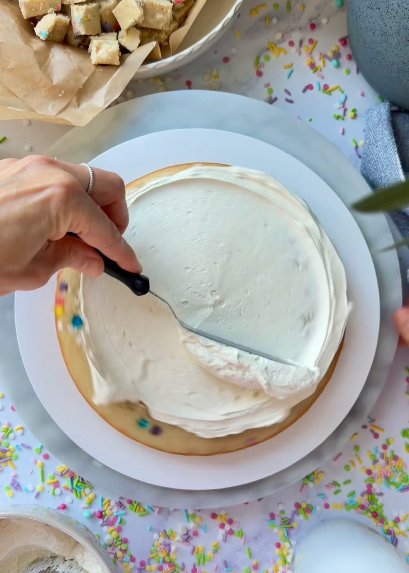 An offset spatula spreading buttercream over the first cake layer