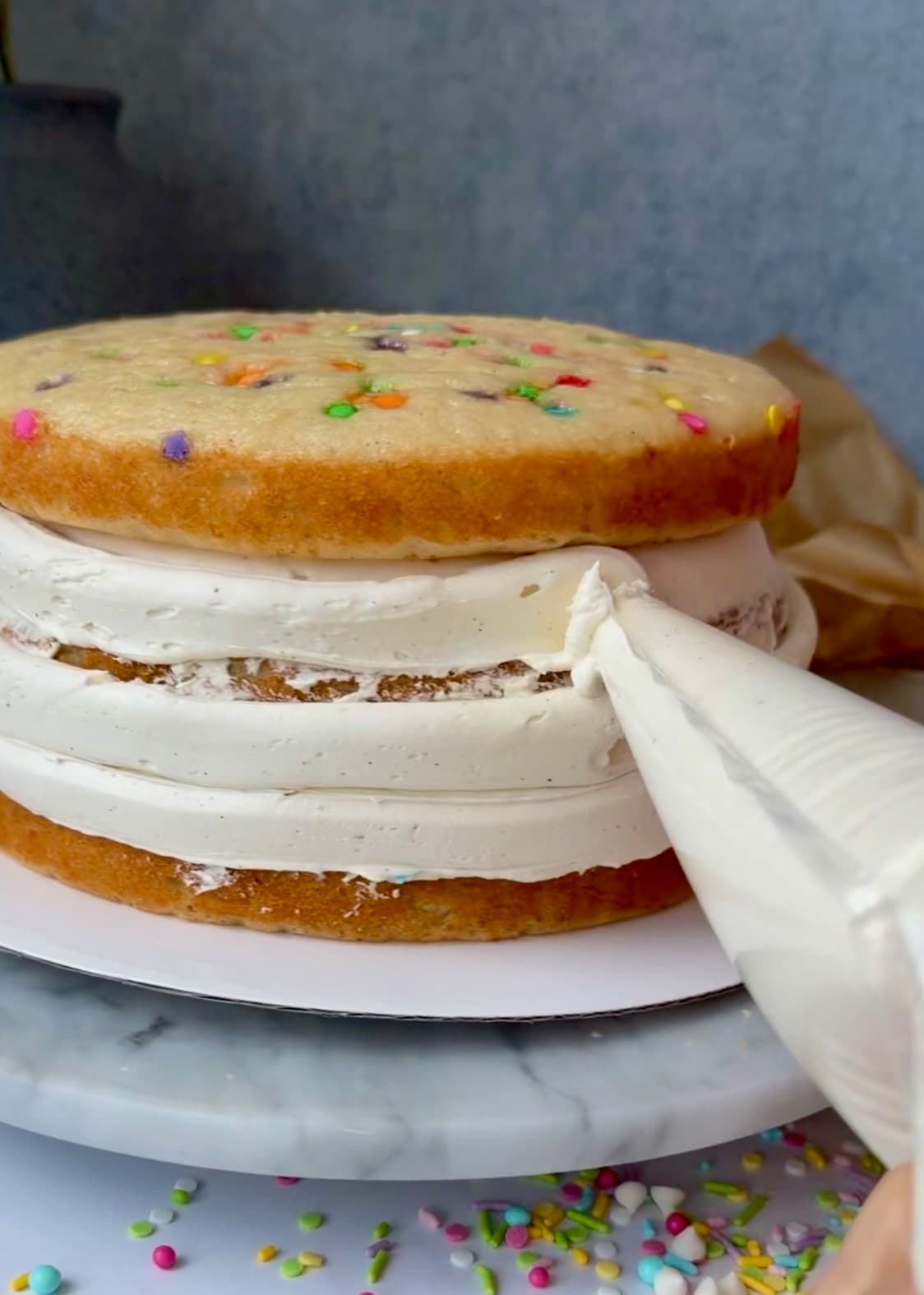 Buttercream being piped around the sides of the stacked cake