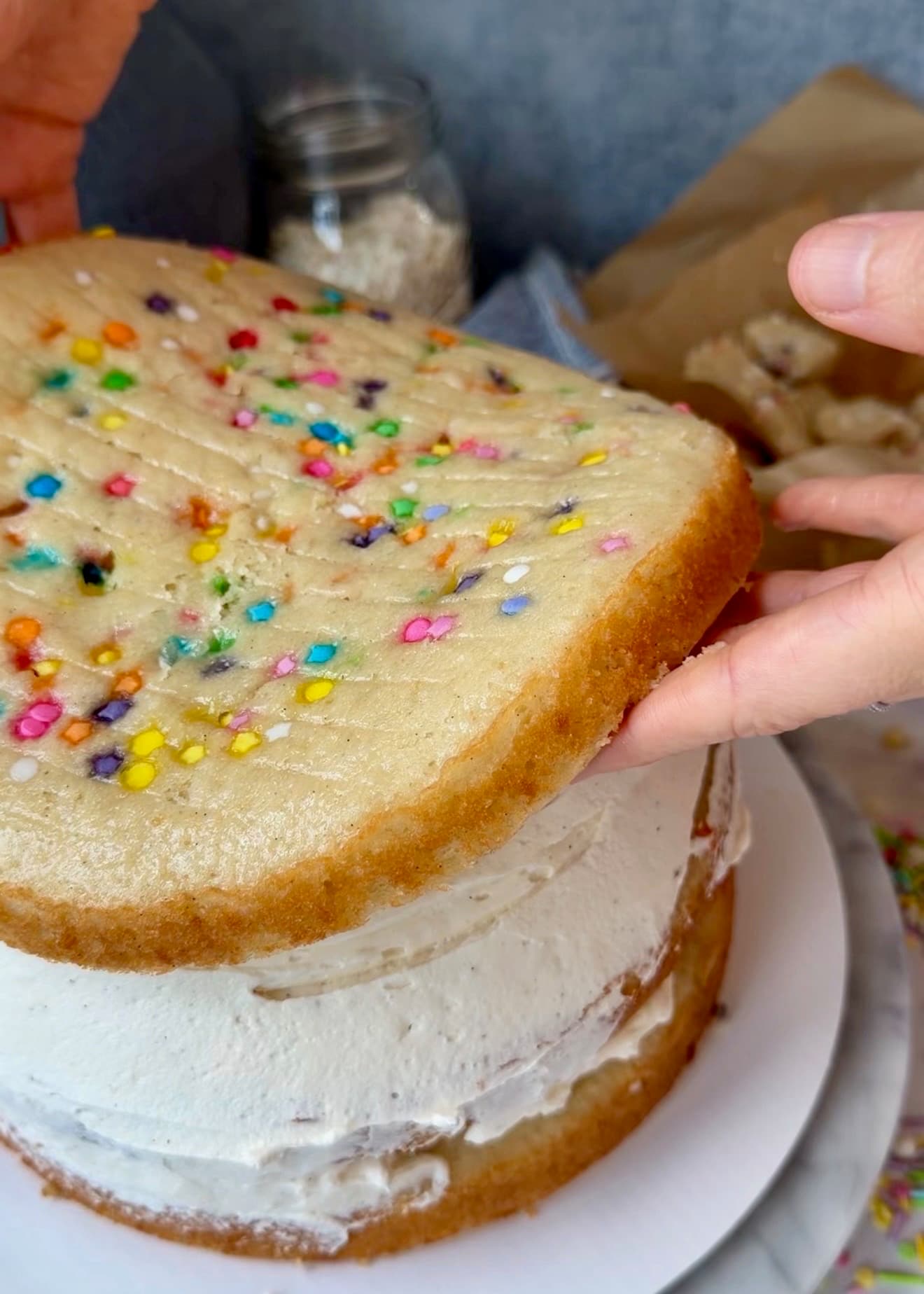 Hands lowering the final cake layer onto the filled stack