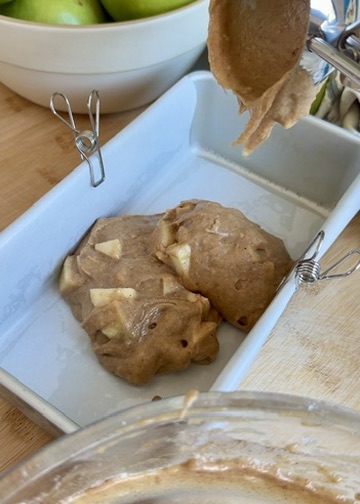 First layer of apple batter being added to a parchment-lined loaf pan