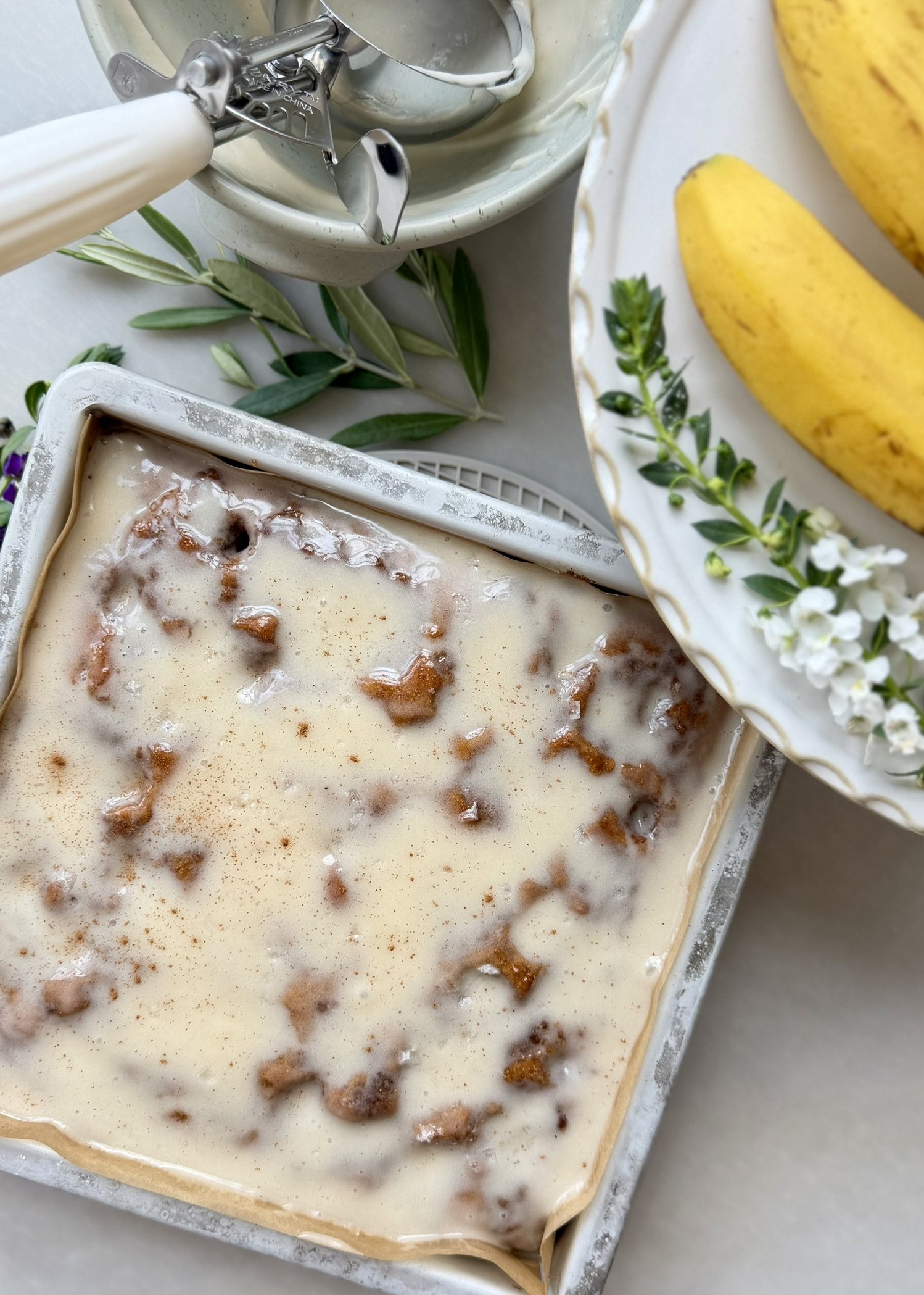 Completed banana cornmeal cinnamon roll poke cake covered with cream cheese icing in a square baking pan