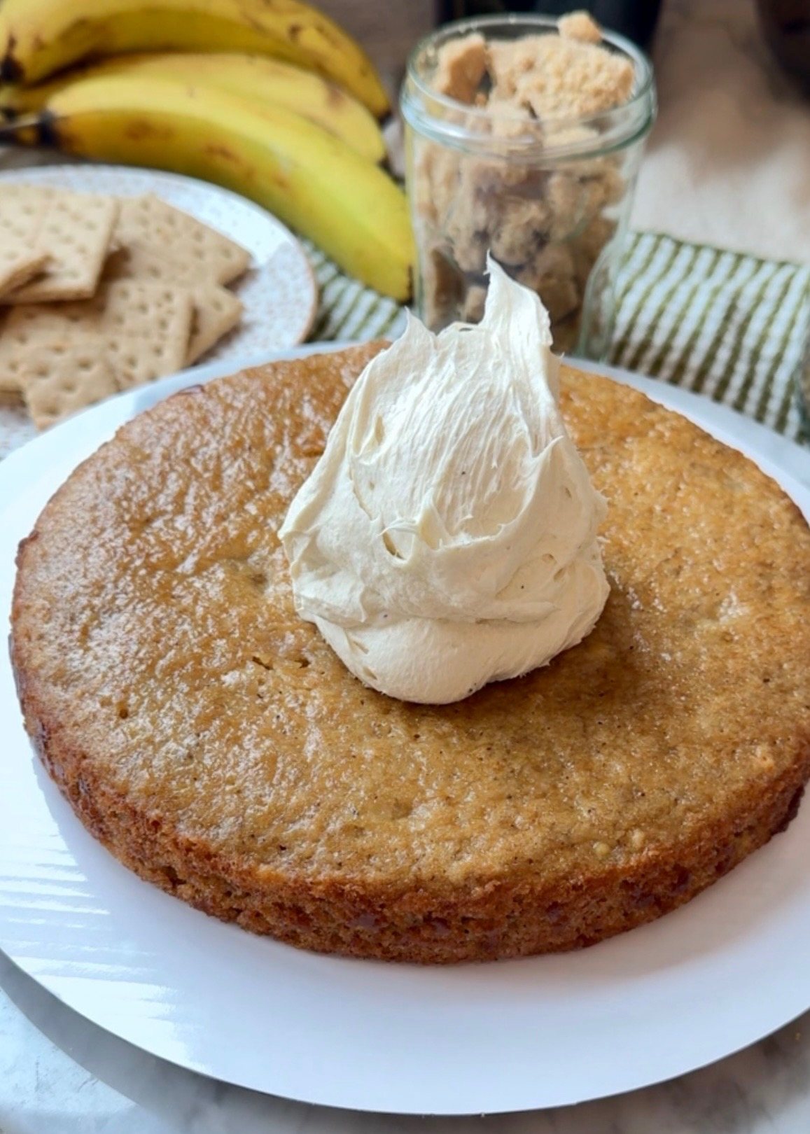 A scoop of cheesecake frosting on a banana cake layer with graham crackers and cookie dough nearby