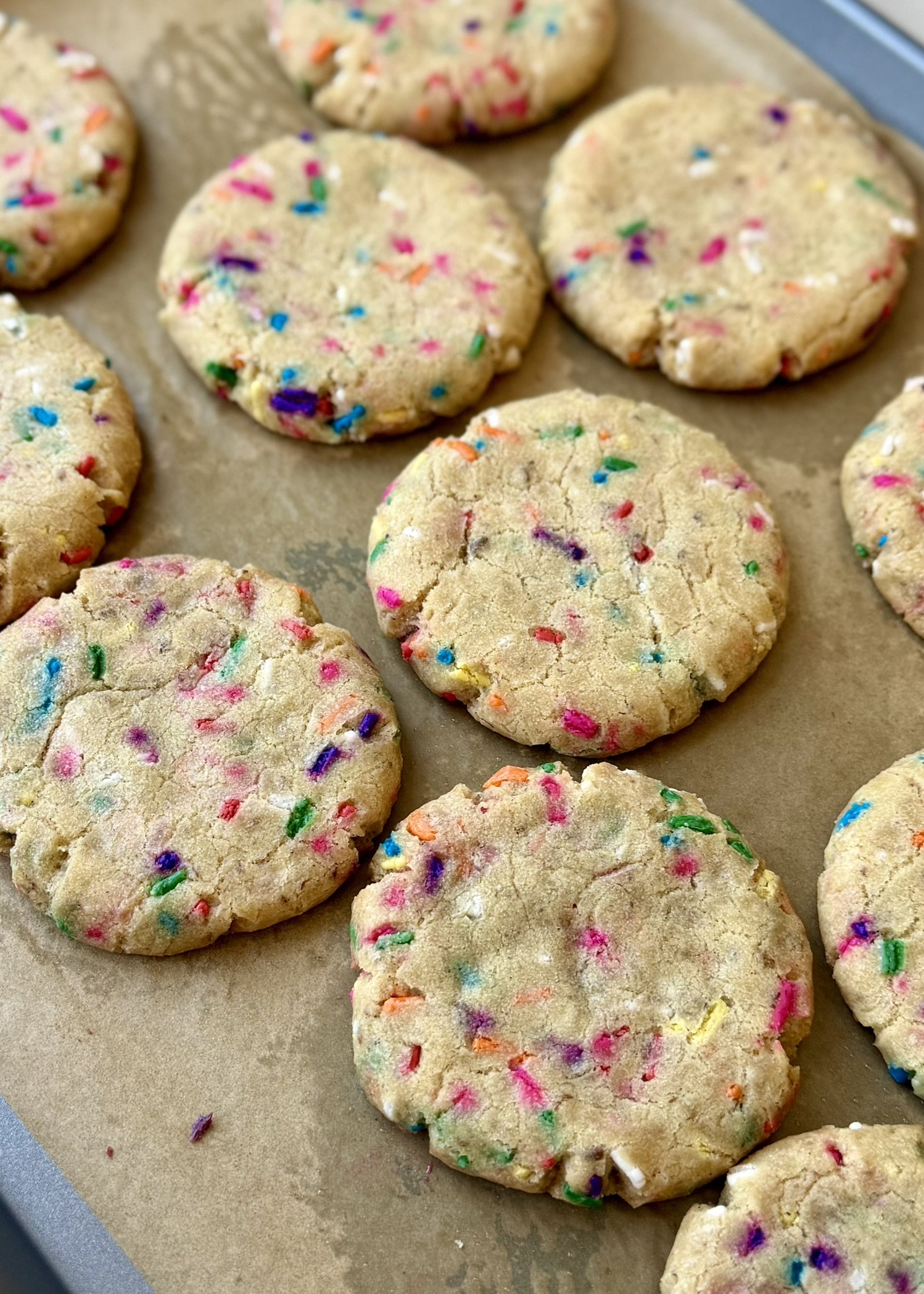Thick unfrosted cake batter cookies filled with colorful rainbow sprinkles cooling on a baking sheet