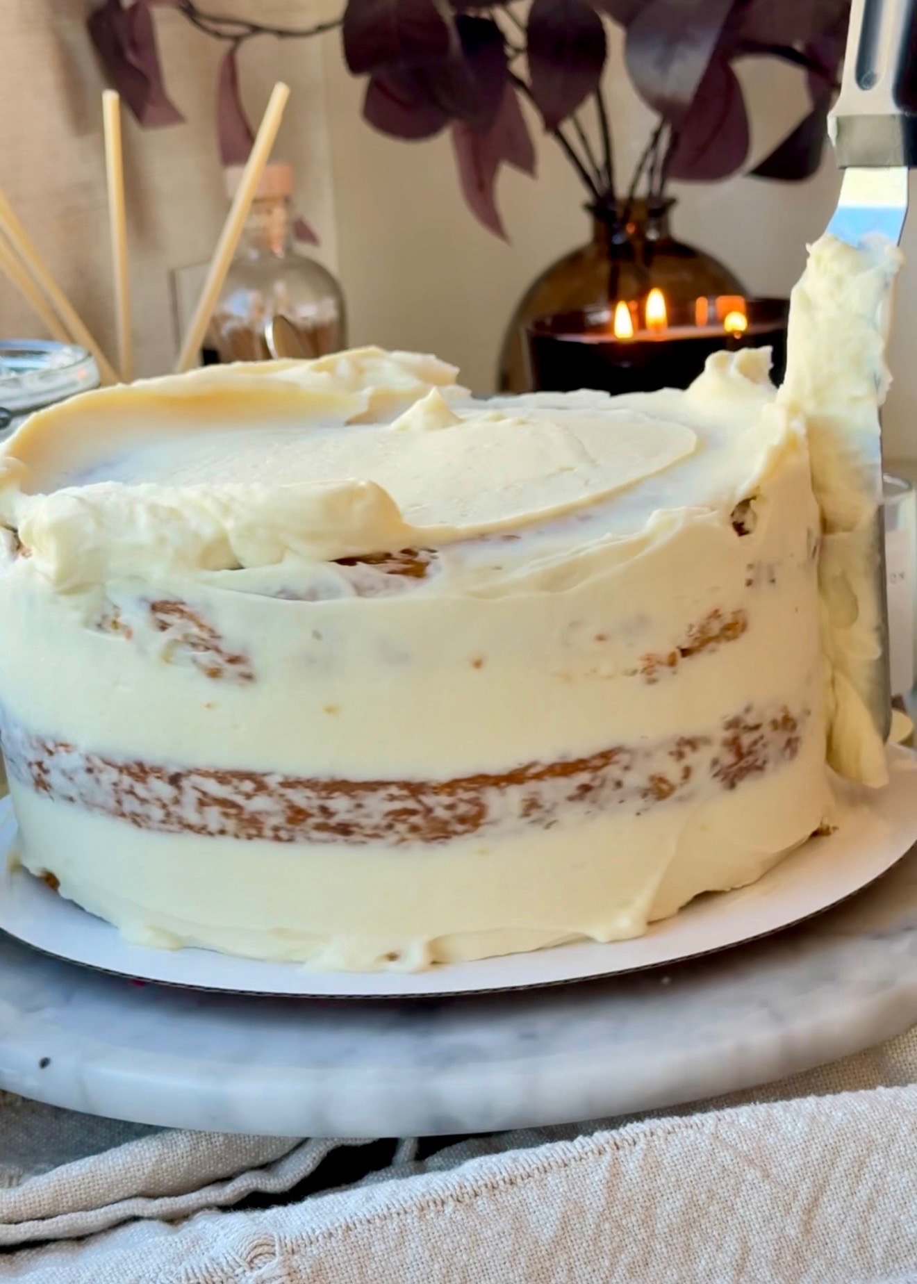 Carrot layer cake being covered with cheesecake frosting