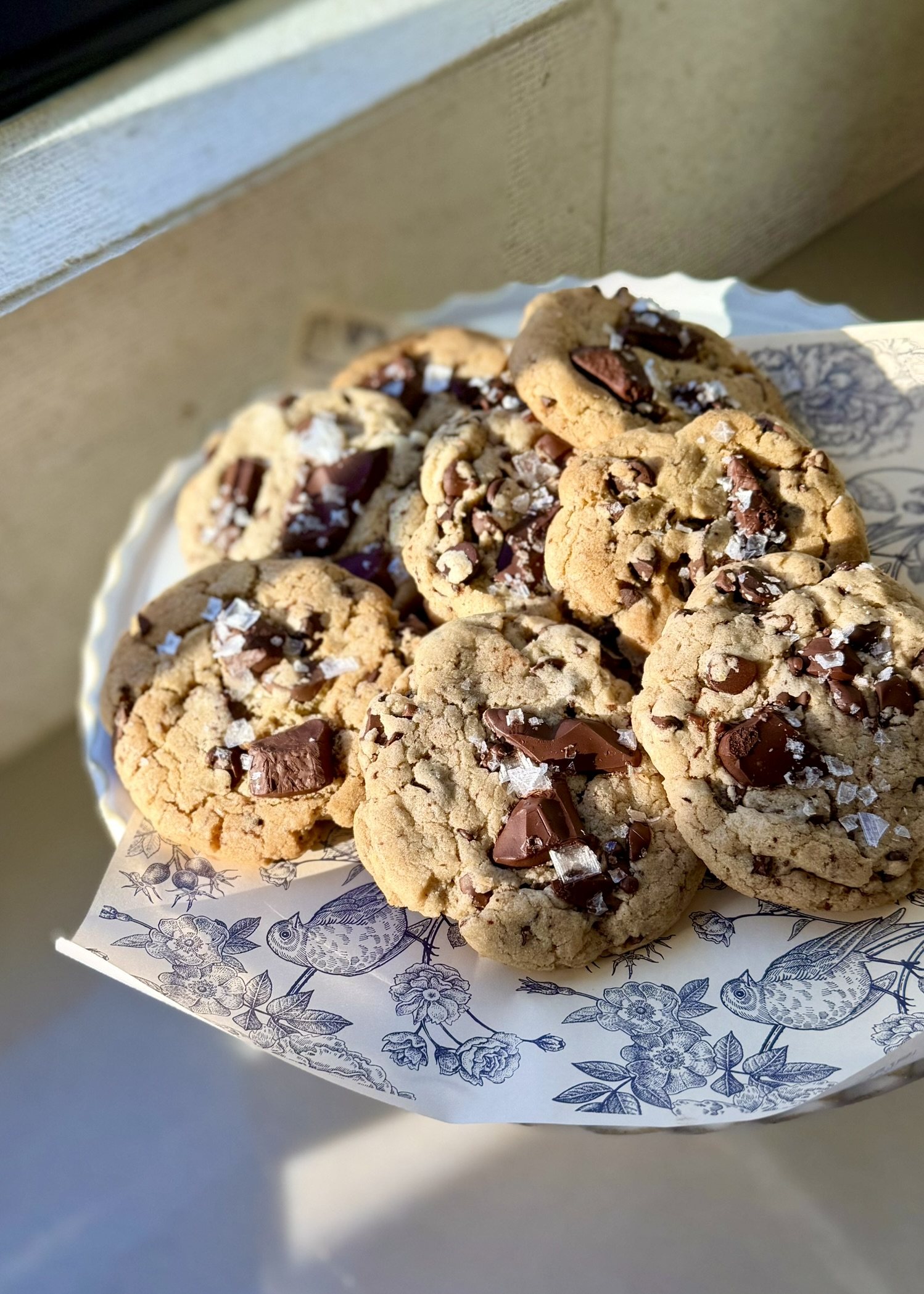 A platter piled with thick chocolate chip cookies finished with chocolate pieces and flaky sea salt