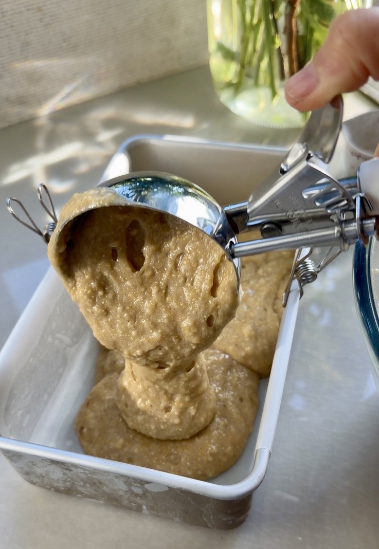 Thick golden cornbread donut loaf batter being poured into a lined loaf pan