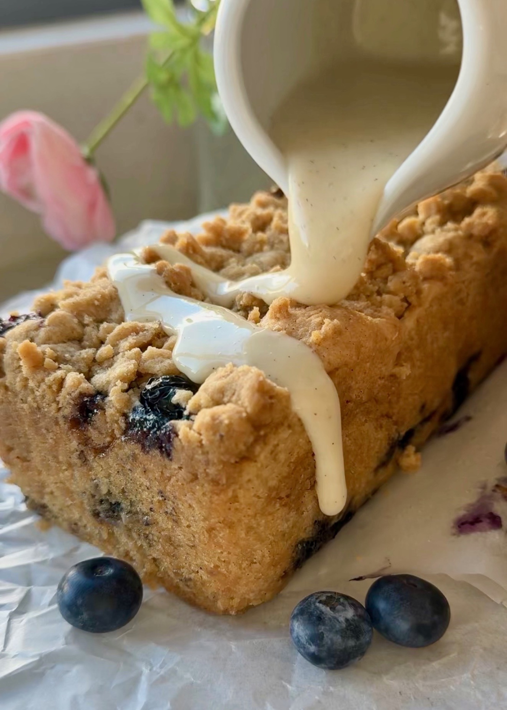 Vanilla bean glaze being poured over a baked Gluten-Free Blueberry Coffee Cake loaf