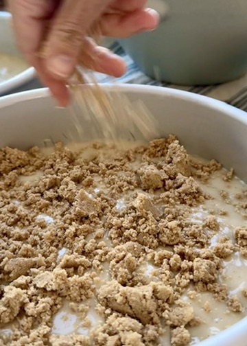 Cinnamon streusel being sprinkled over vanilla cake batter