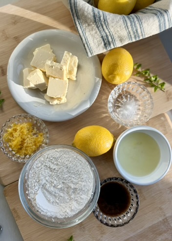 Lemon loaf ingredients arranged with fresh lemons, flour, butter, sugar, oil, and vanilla bean paste