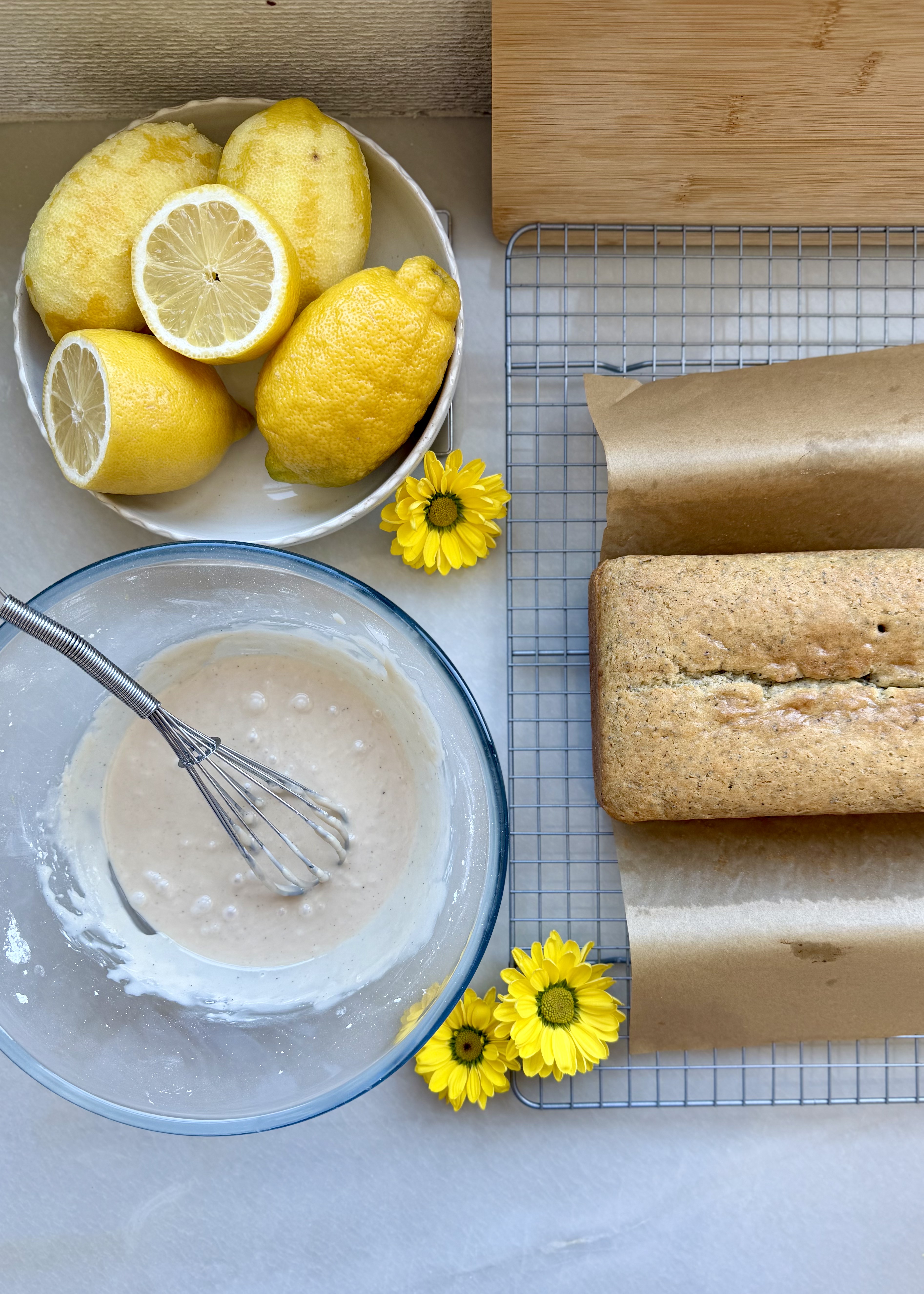 Lemon poppy seed loaf beside fresh lemons and a bowl of vanilla glaze