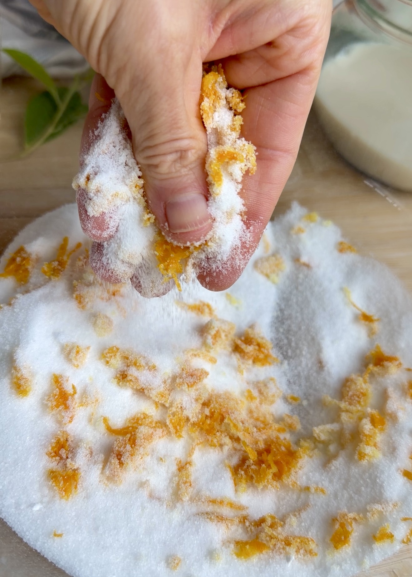 Fresh orange zest being rubbed into granulated sugar