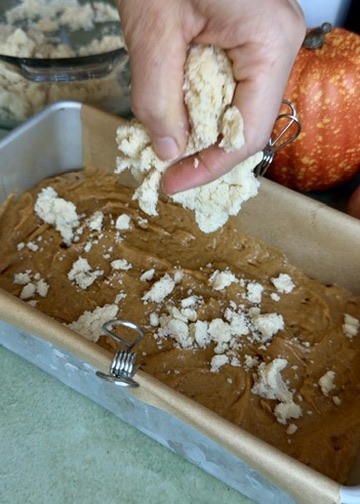 Buttery streusel being added over pumpkin spice donut loaf batter