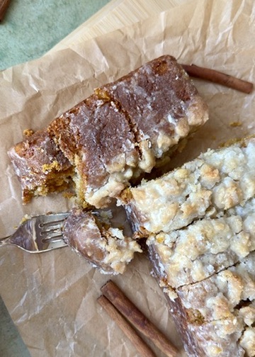 Slices of glazed Pumpkin Spice Old-Fashioned Donut Loaf on parchment with cinnamon sticks