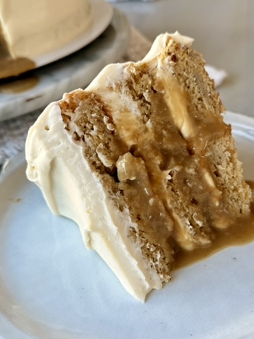 Upright slice of banana cheesecake cake covered with salted caramel