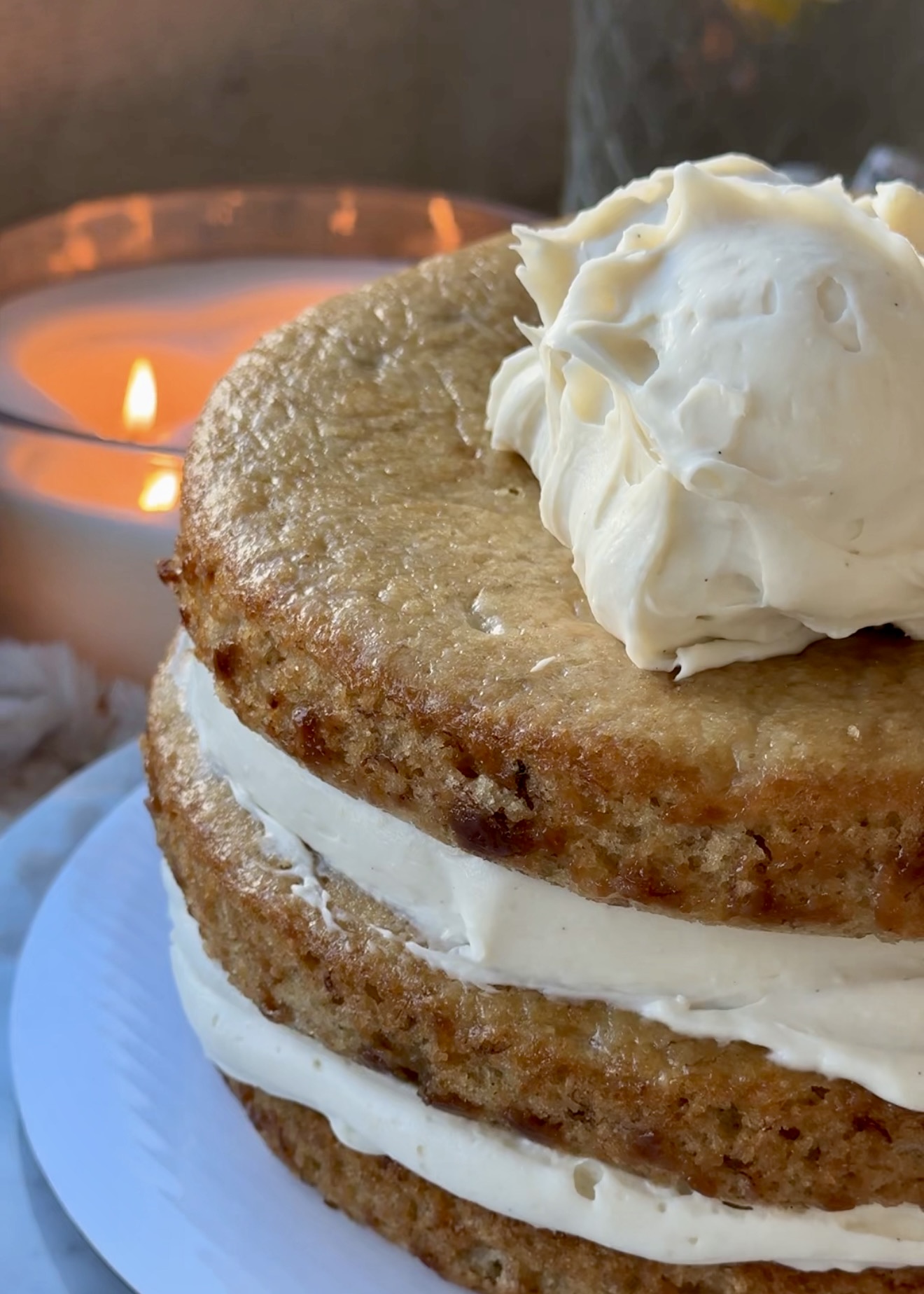 Stacked banana cake layers being covered with cheesecake frosting