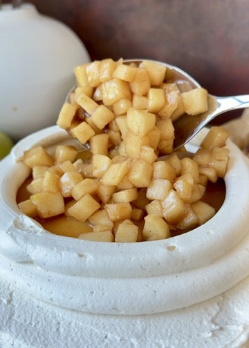 Spoonful of apple filling being added over salted caramel inside a buttercream dam