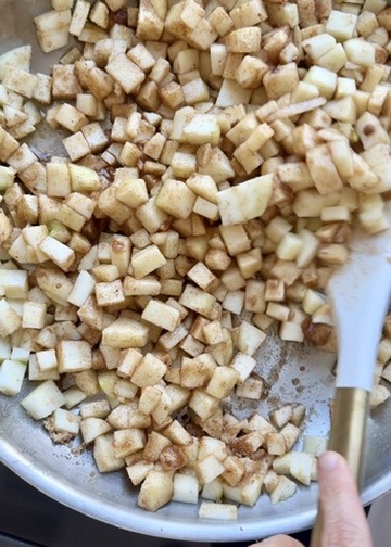 Diced Granny Smith apples cooking with brown sugar and spices in a stainless steel skillet