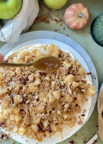 Salted caramel being spooned over apples and pecan streusel on the finished cake