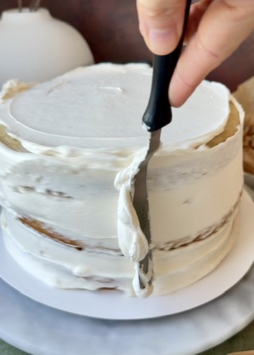 Thin layer of vanilla bean buttercream being spread over the assembled cake