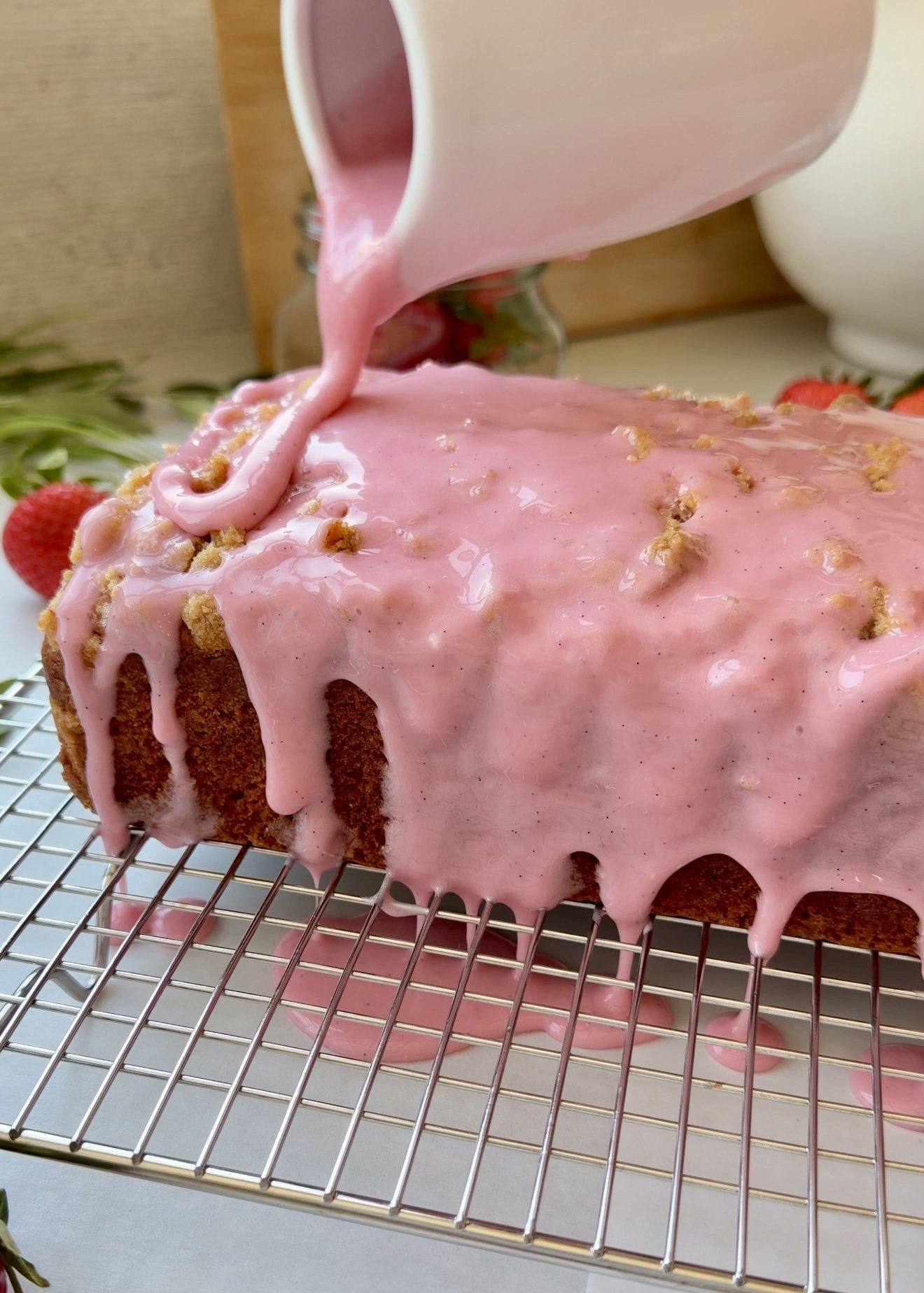 Pink vanilla glaze being poured over a strawberry old-fashioned donut loaf