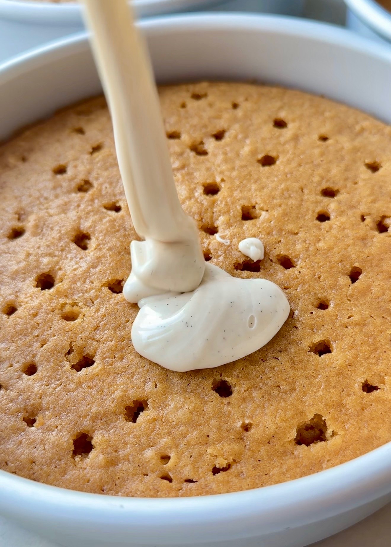 Vanilla bean glaze pouring over a warm sweet potato cake layer